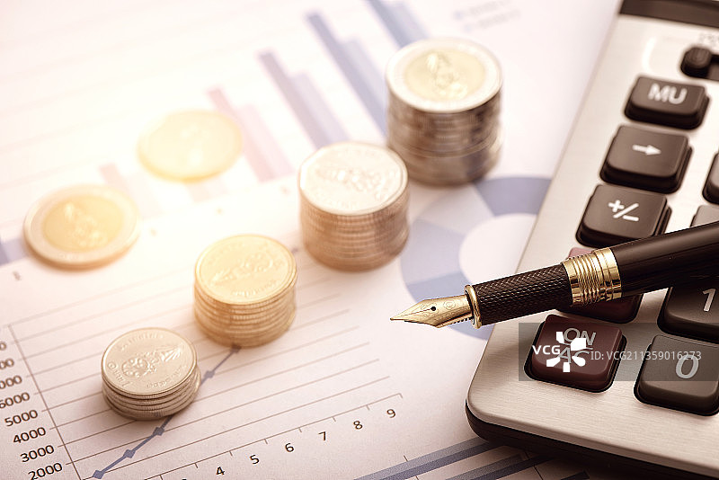放在财务数据报表上的硬币、计算器和钢笔图片素材