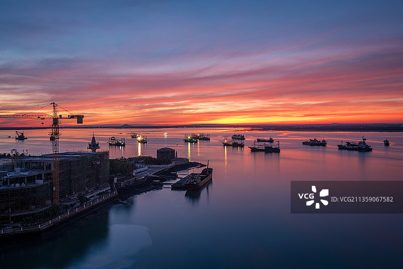 黎明的晨光中，迎着绚丽多彩的朝霞，大小不一的船只在港口忙碌着图片素材
