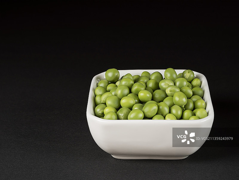 黑色背景下，桌上碗中绿豌豆特写图片素材