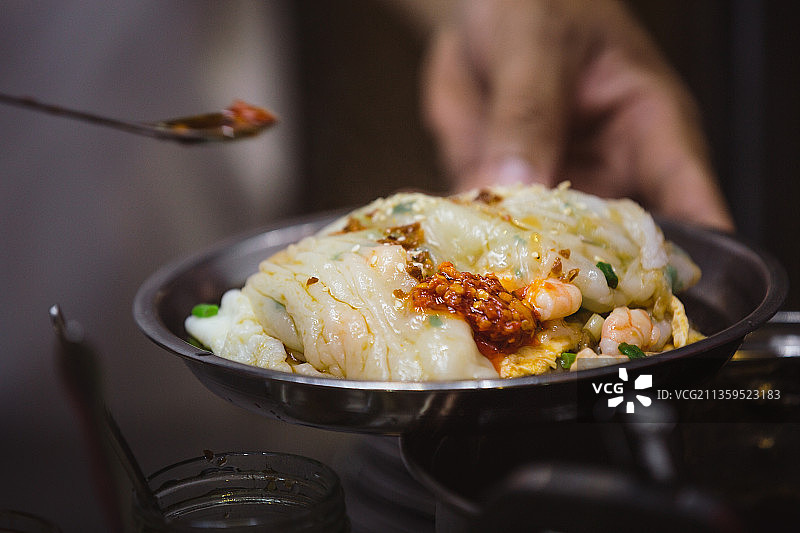 一碗正在添加辣椒调料的肠粉图片素材