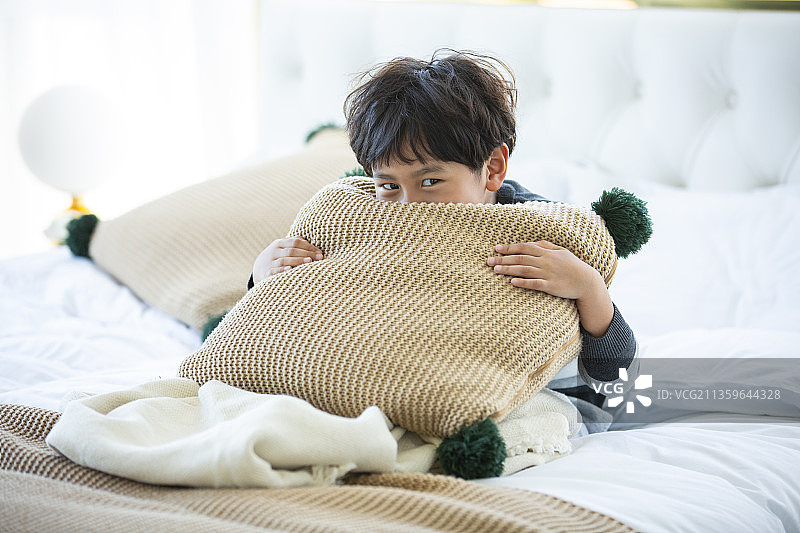 小男孩在卧室床上抱着靠枕图片素材