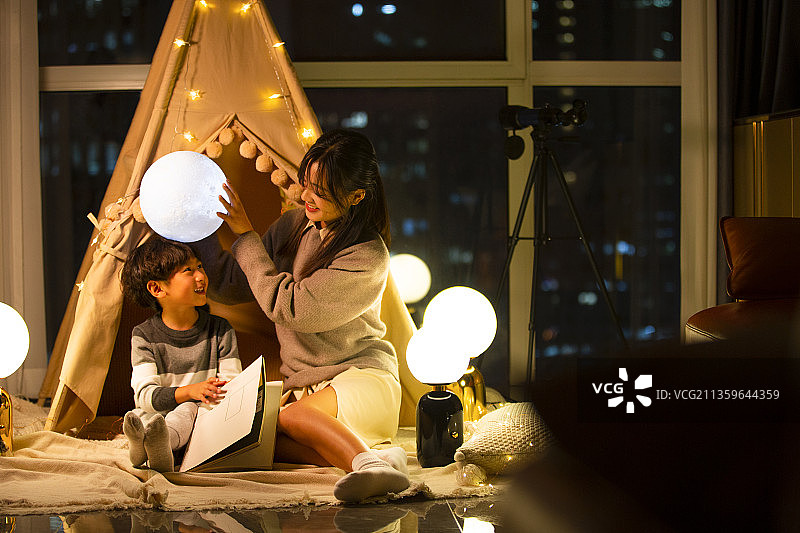 快乐母子在客厅搭帐篷露营，妈妈拿着月球灯举到小男孩的头顶图片素材