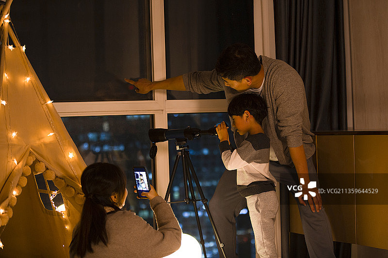 一家三口在客厅使用天文望远镜和手机拍照录像图片素材