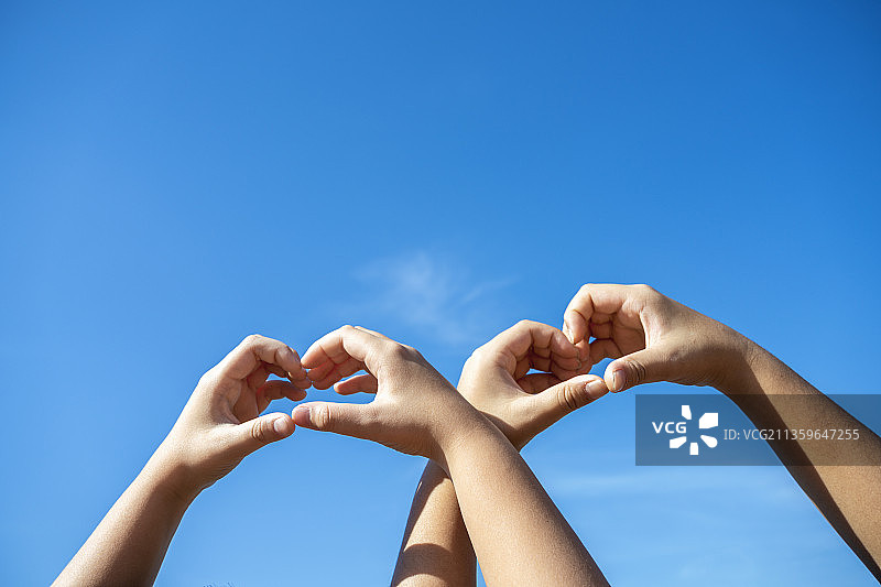 两双爱心手势的手臂伸向蓝色天空图片素材