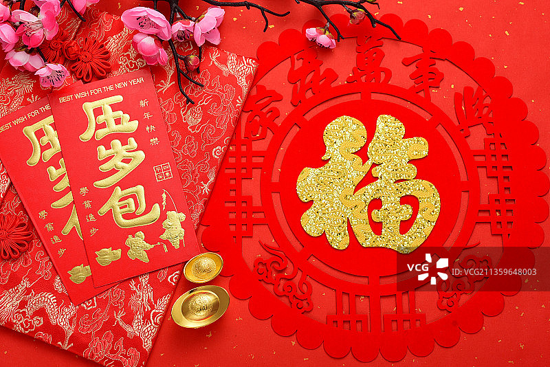 摆放在红色背景纸上的腊梅、福字贴纸、红包和元宝图片素材