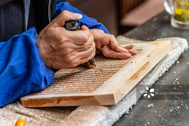 老人手拿着刻刀在木板上雕刻版雕图片素材