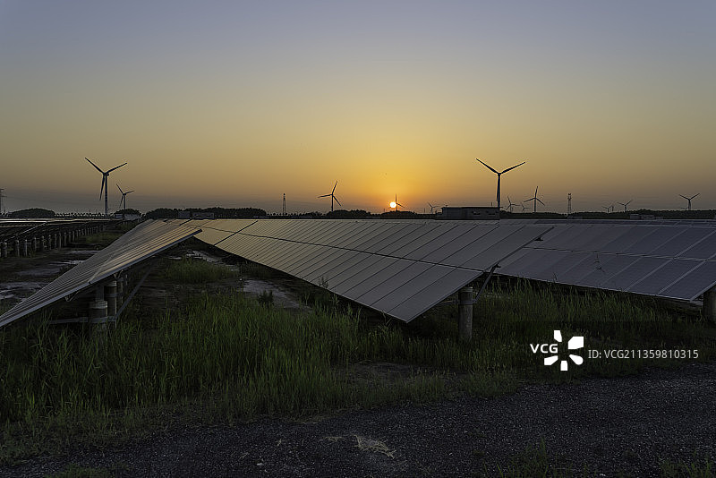 日落时的太阳能电池装置和风力发电机。带有光伏板和风力涡轮机的发电装置。清洁能源和碳中和概念。图片素材