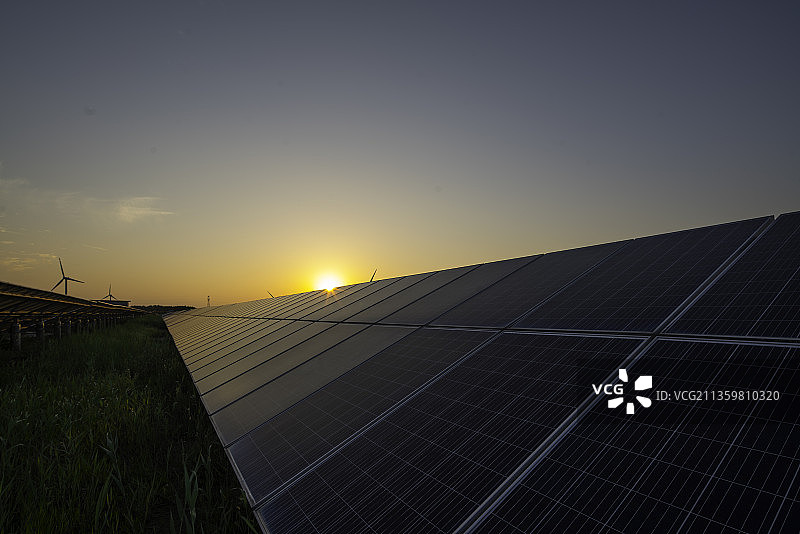 日落时的太阳能电池装置和风力发电机。带有光伏板和风力涡轮机的发电装置。清洁能源和碳中和概念。图片素材