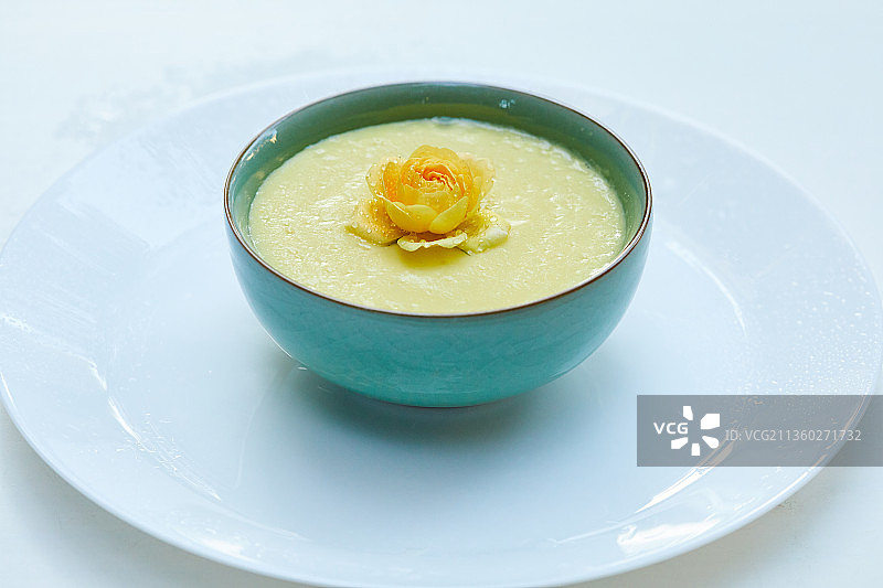 花园里白色餐桌上的一碗有黄色花朵的有机素食玉米羹图片素材