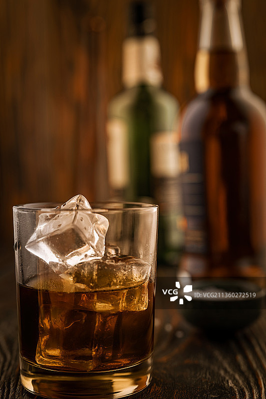 一杯加冰威士忌，木质背景上有酒瓶图片素材