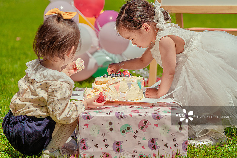 两个小女孩分享公园草坪生日派对的生日蛋糕图片素材