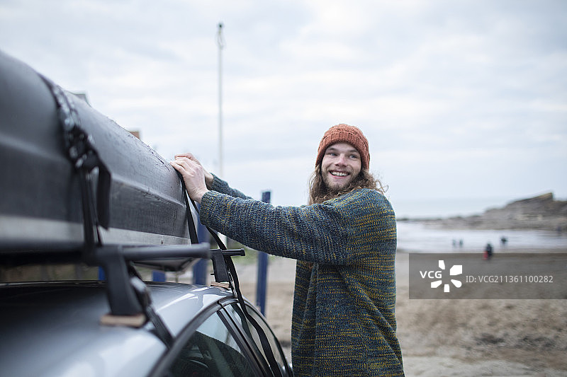 面带微笑的年轻男人在海滩上将独木舟固定到汽车上图片素材