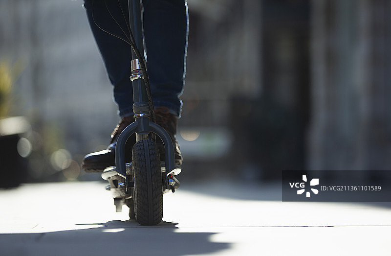 阳光明媚的人行道上骑电动滑板车的男人图片素材