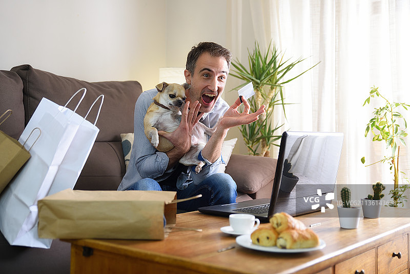 兴奋的男人在家和他的狗一起网上购物图片素材