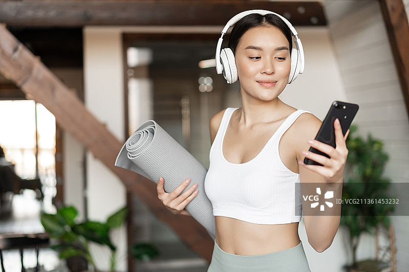 年轻亚洲女性戴着耳机在家中站立，听音乐图片素材