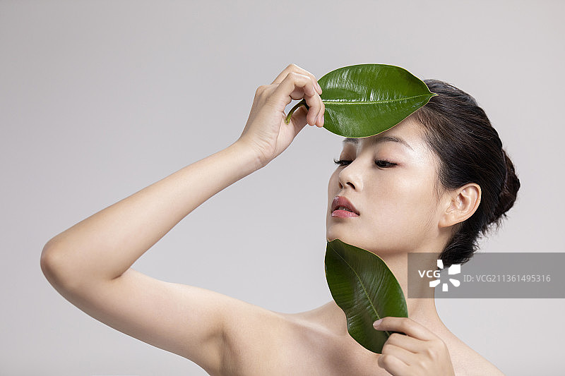 漂亮的年轻女子拿着两片绿叶图片素材