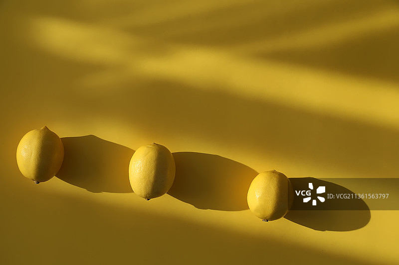 黄色背景上的三个黄色柠檬及其阴影图片素材