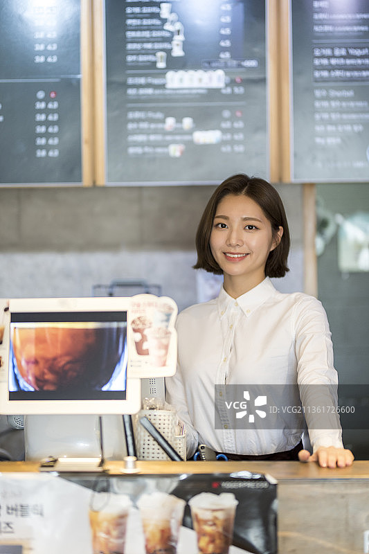 站在咖啡馆收银台旁的微笑女人图片素材