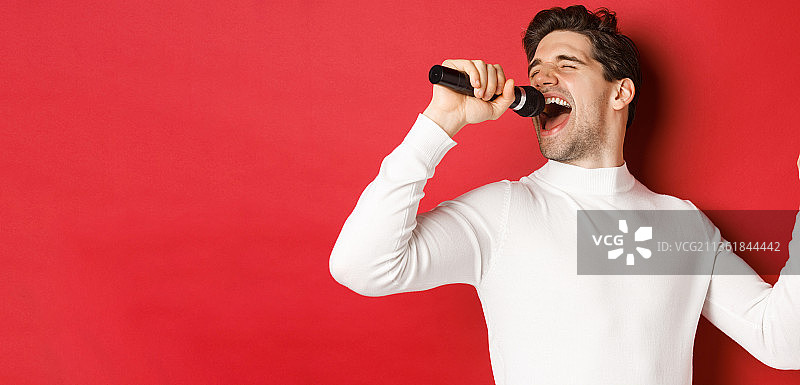 穿着白色毛衣的英俊男人，拿着麦克风唱歌图片素材