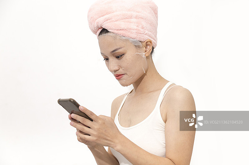 一名东方女人一边敷面膜一边看手机图片素材