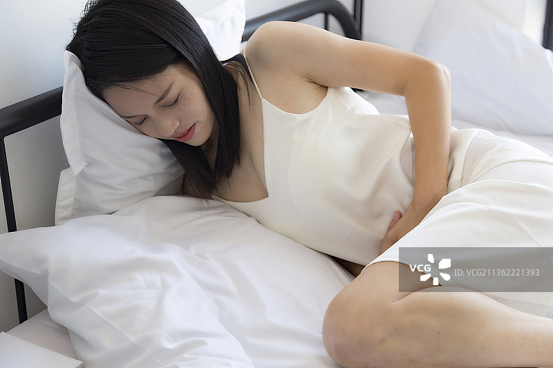 一个在床上肚子疼的东方女人图片素材