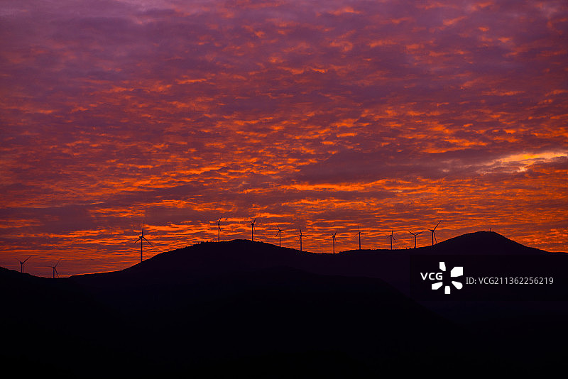 风力发电机，橘色天空下山脉的剪影图片素材