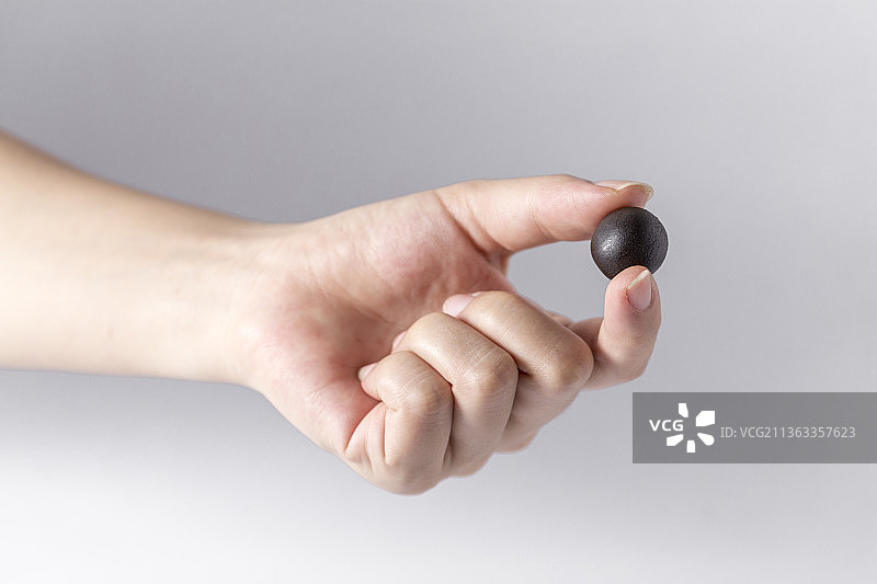 白色背景一只手拿着一颗中成药药丸特写图片素材