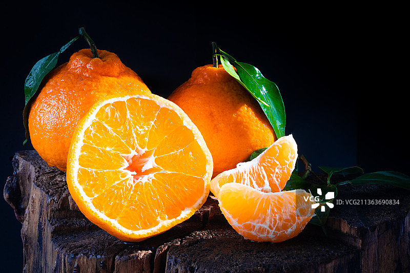 黑色背景前的树桩上放着几个丑橘图片素材
