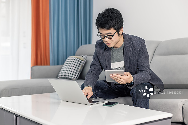 年轻男性在家庭坐沙发上用平板电脑办公图片素材