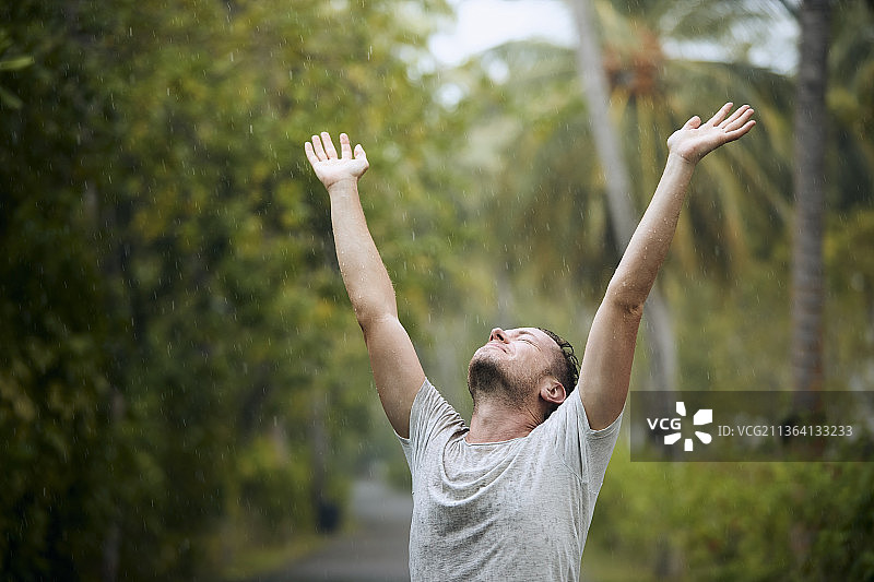 男子享受大雨，张开双臂站在树林中图片素材
