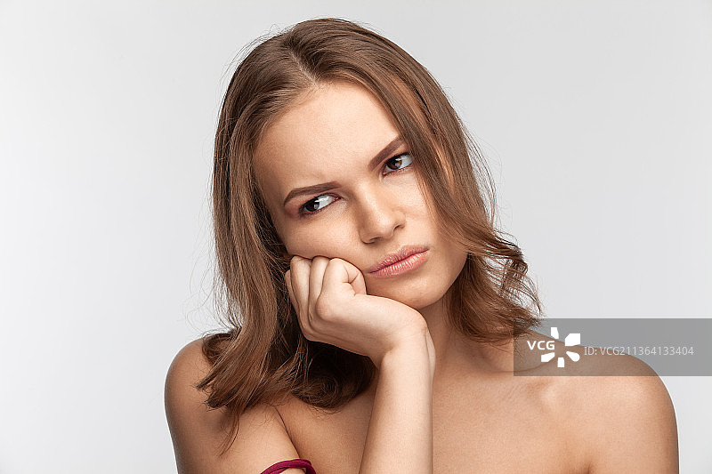 面带不悦的可爱棕发女孩，影棚肖像图片素材