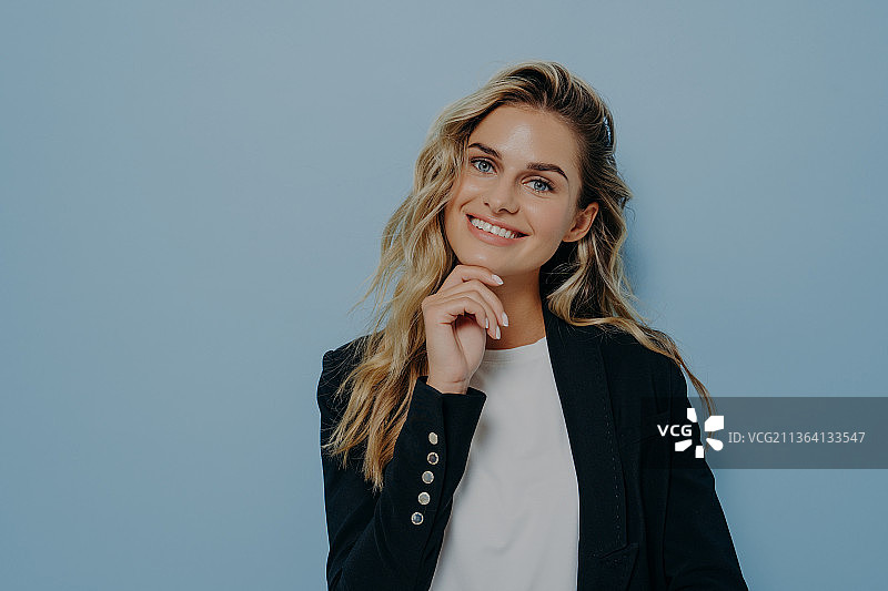手托下巴对着镜头微笑的年轻金发女人图片素材