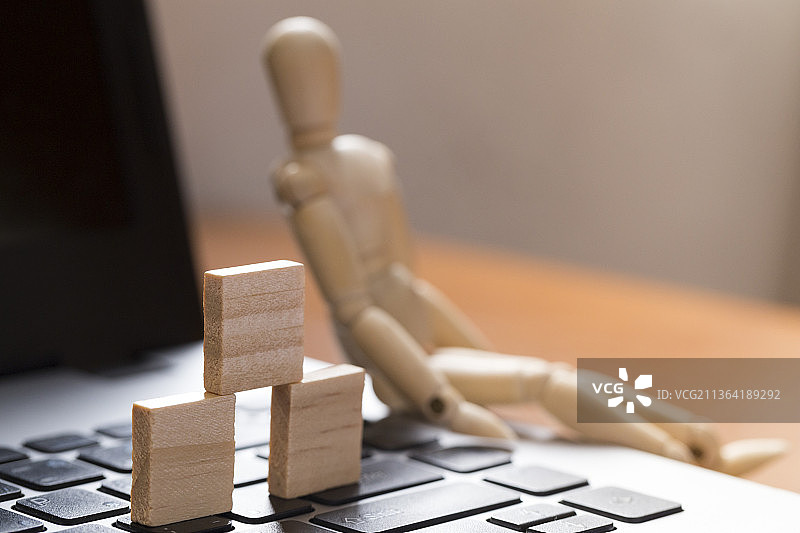侧逆光的手提电脑与木人偶木方块局部特写图片素材
