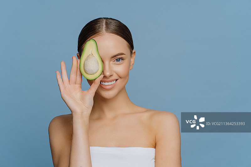 用半个鳄梨遮住眼睛的快乐美丽的女人图片素材