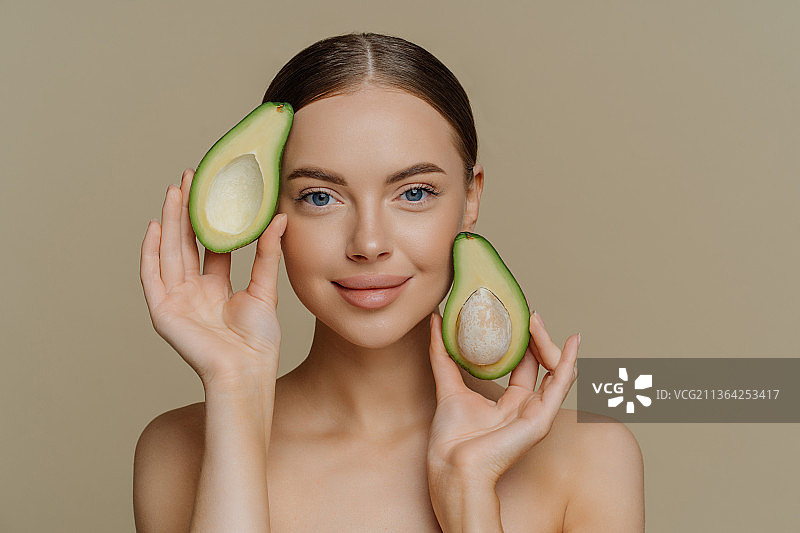 表情温柔地看着镜头，手拿半个鳄梨的女人图片素材