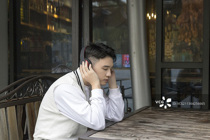 一个男青年在咖啡厅户外座位上看手机听音乐图片素材