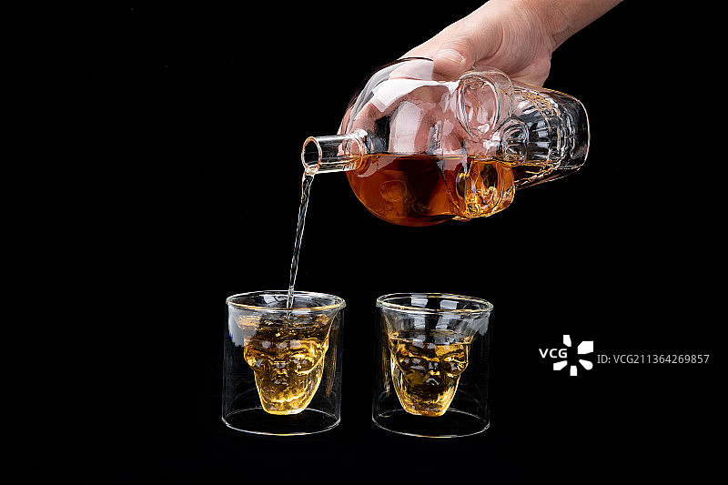 手拿着骷髅酒瓶给酒杯倒酒图片素材