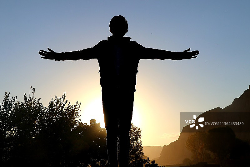 在孤独中寻求慰藉：日落时分，男子张开双臂，眺望天空图片素材