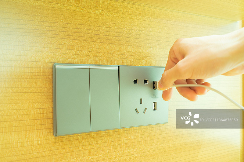 中国卧室的床头柜上方的插座面板和电灯开关，手持一根充点钱插入USB端口图片素材