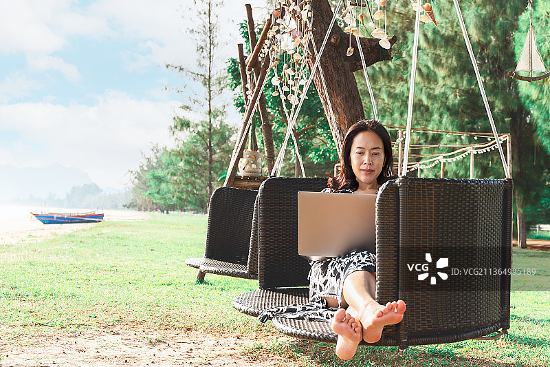 坐在海滩吊床上用笔记本电脑工作的美女图片素材