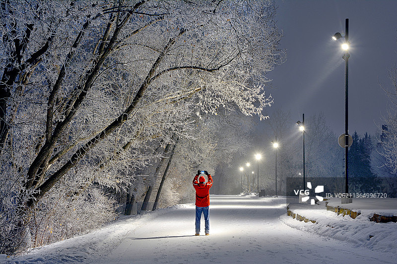 寒冷的冬日拂晓，男子站在加拿大艾伯塔省卡尔加里白雪覆盖的道路上图片素材