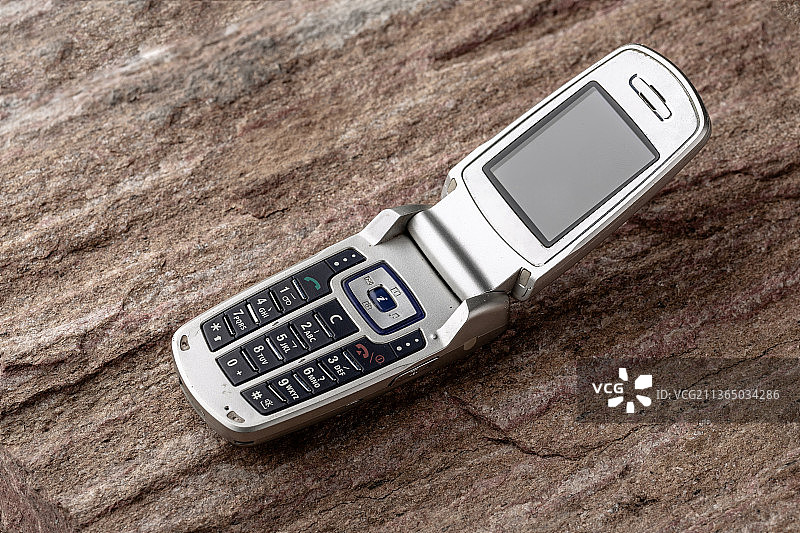 一个老旧的翻盖手机放在石头上图片素材