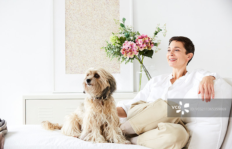 一位成熟的满足女性和她可爱的小狗在沙发上的肖像图片素材
