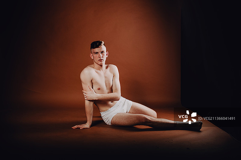 身穿白色内衣的年轻男人，无上装在黑色背景下锻炼图片素材