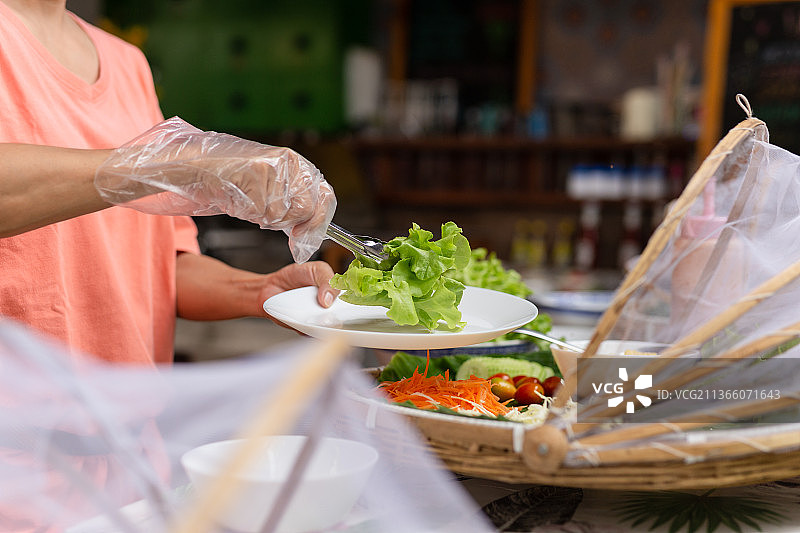女人戴手套在自助餐上取生菜图片素材