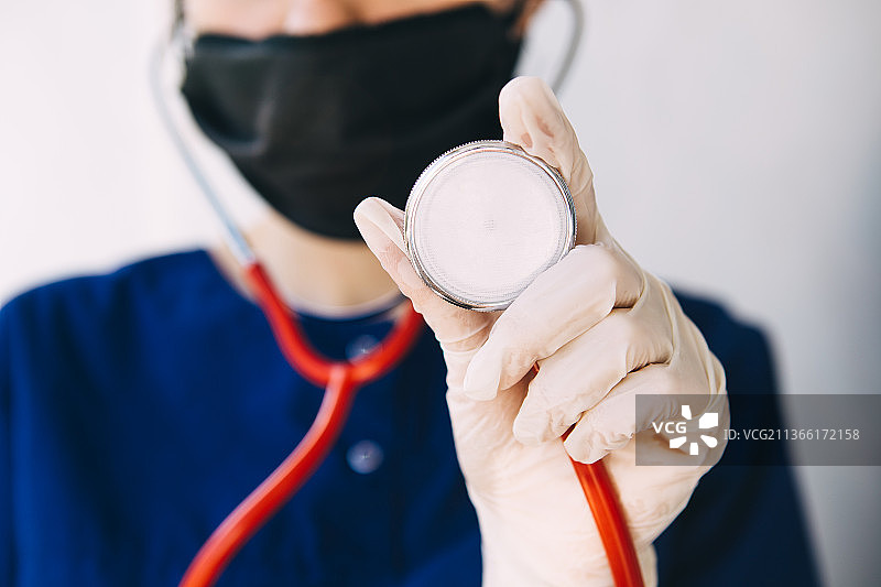 穿着手术服、戴着手套和口罩的年轻医生拿着红色听诊器图片素材