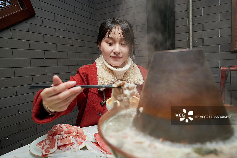 在饭店吃传统铜锅涮肉的亚洲少女图片素材