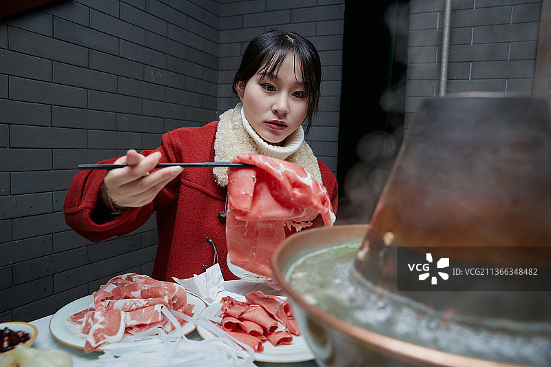 在饭店吃传统铜锅涮肉的亚洲少女图片素材