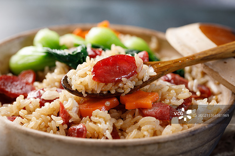 从煲仔饭中舀取一勺米和一片腊肠图片素材