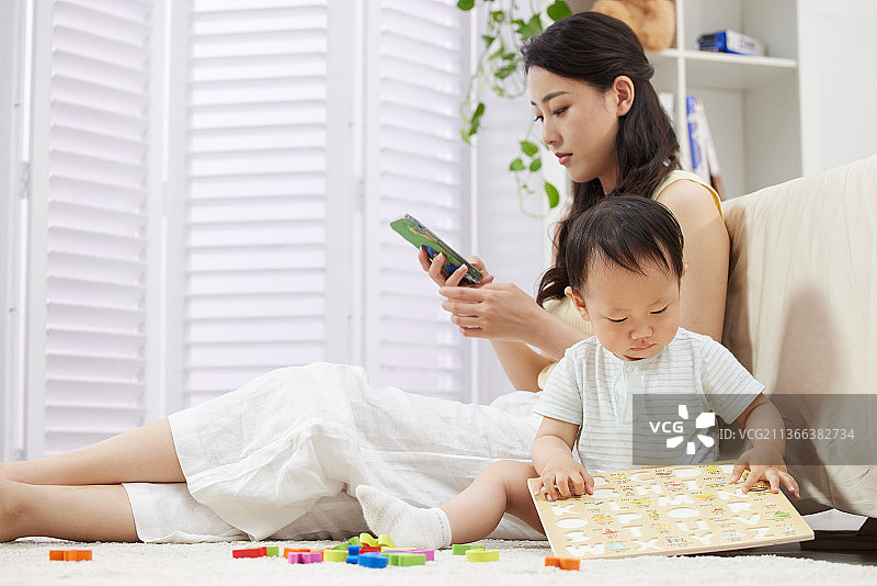 陪着宝宝玩耍的年轻妈妈使用手机图片素材